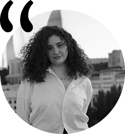 Tuğla duvarın yanında duran, resmi kıyafet giymiş ve elinde bir fincan tutan iş kadını.