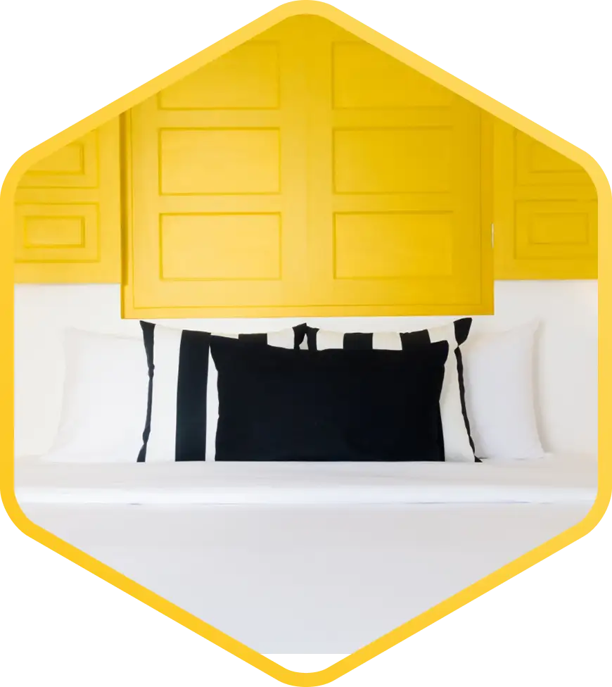 Modern bir iç tasarımda beyaz yatak, siyah yastıklar ve sarı duvar panelleriyle donatılmış minimalist yatak odası.